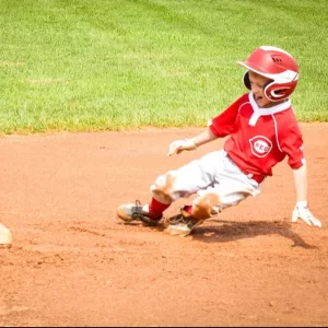 Youth baseball player sliding into a base on a dirt field.