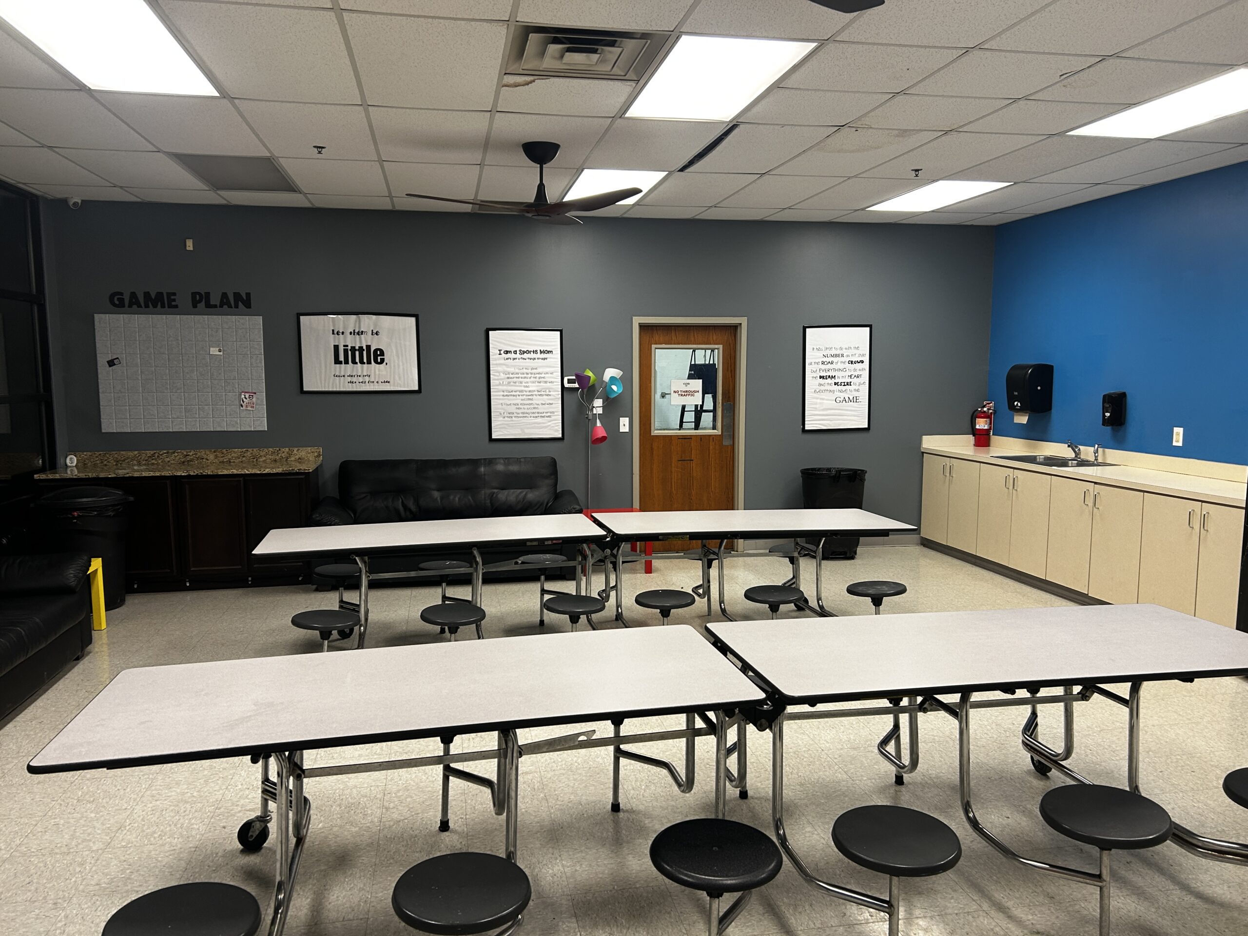 Indoor party room at The Yard featuring folding tables with stools, lounge seating, cabinets, and a blue accent wall.