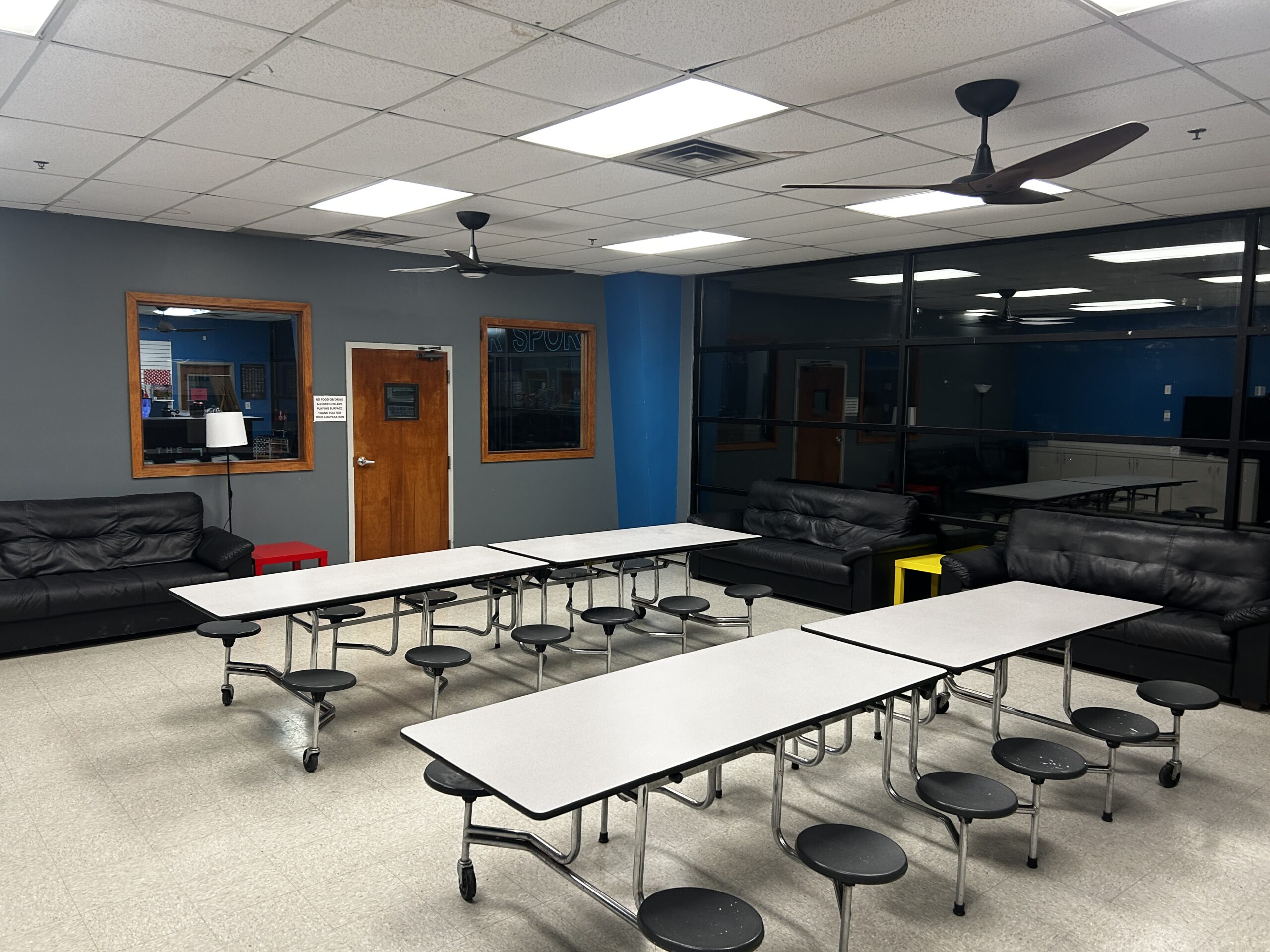 Indoor party room at The Yard featuring folding tables with stools, lounge seating, cabinets, and a blue accent wall.